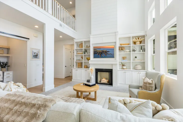 Open-concept living space anchored by a gas fireplace with custom built-in cabinetry, white shaker-style cabinetry with glass-front upper shelving, and integrated shelving displaying decorative accents