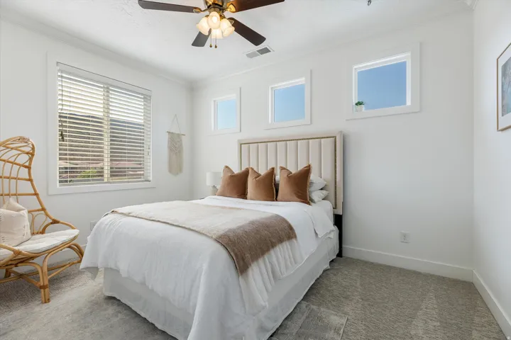 Bright secondary bedroom featuring a wood-framed bed, layered white bedding, and multiple windows flooding the space with natural light