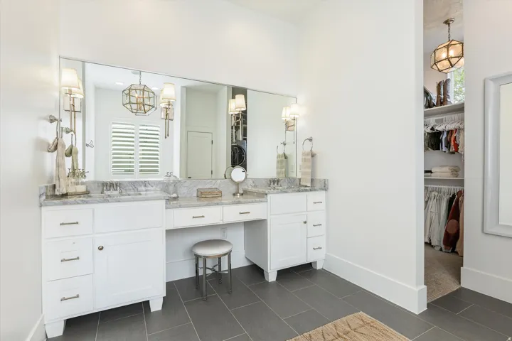 Luxurious primary bathroom featuring dual vanities with white cabinetry, polished countertops, and an expansive illuminated mirror