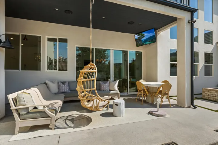 Expansive covered patio with polished concrete flooring, featuring multiple seating areas and woven rattan hanging chair