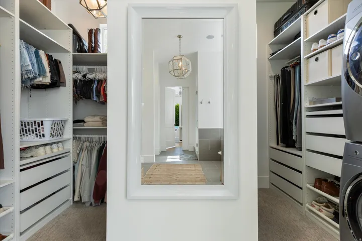 Luxurious walk-in closet featuring custom white cabinetry with integrated drawers, open shelving for folded garments and accessories, and a full-length mirror