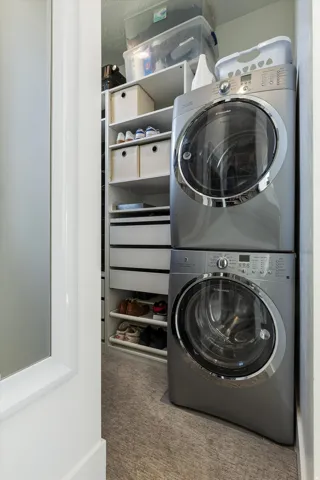 Dedicated laundry room featuring stacked front-load washers and dryers in stainless steel, complemented by built-in shelving with storage containers and woven baskets for organized linen and supply storage