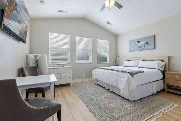 Spacious primary bedroom featuring hardwood flooring, a wood-finish bed frame with upholstered headboard, built-in wooden nightstands, and a geometric area rug