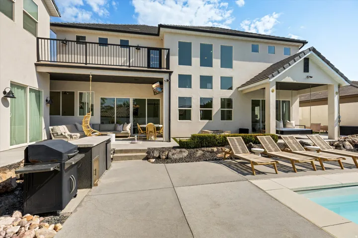 Expansive outdoor living space featuring a resort-style swimming pool, concrete patio with lounge seating areas, built-in gas grill with countertop workspace, and covered pergola structure