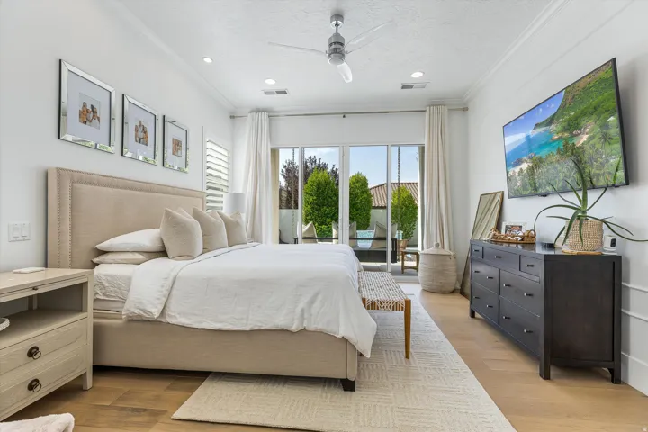 Bright, light-filled primary bedroom featuring a wood-finish plank floor, neutral upholstered bed frame with coordinating pillows, dual nightstands with drawer storage, and a ceiling fan with recessed lighting