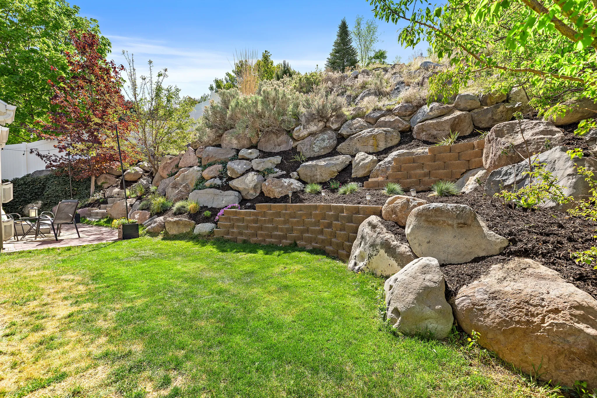 Expansive lawn area with a stone retaining wall and tiered landscaping