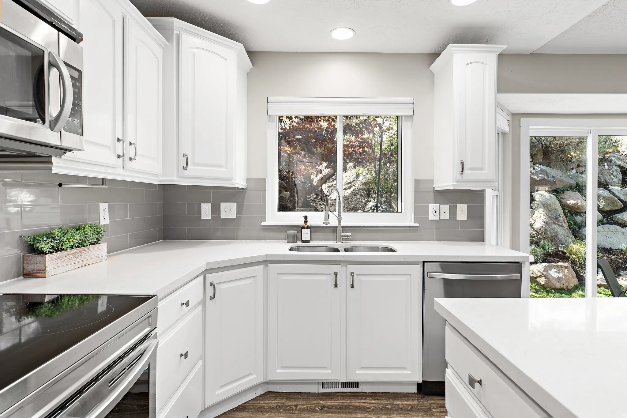 Bright kitchen featuring crisp white cabinetry, stainless steel appliances, and a white quartz countertop with waterfall edge
