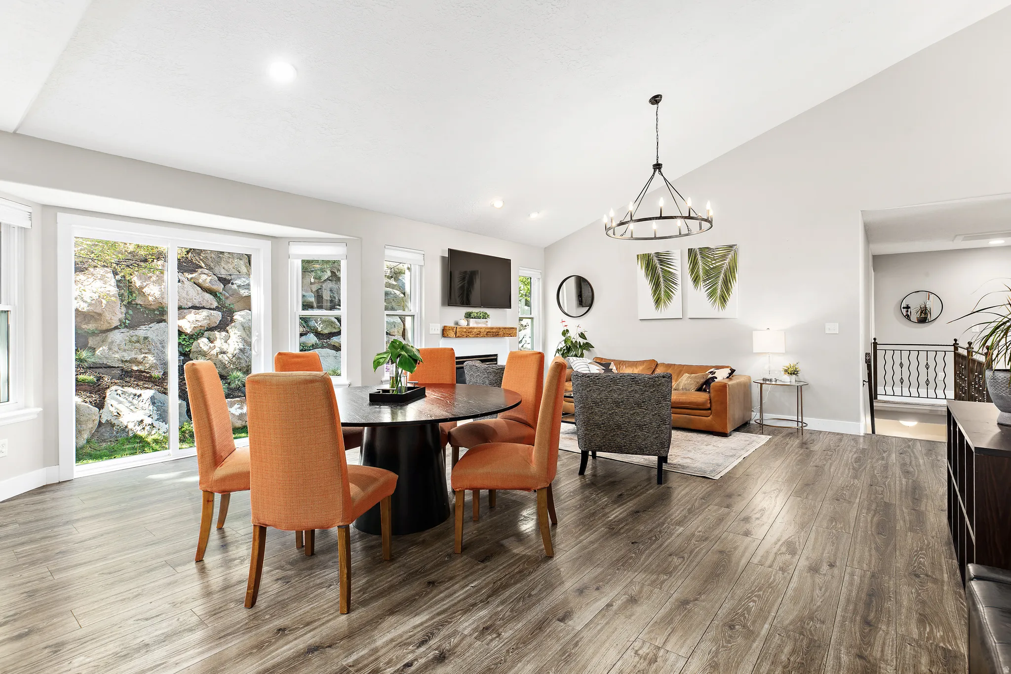 Open-concept living area featuring wood-finish flooring, vaulted ceilings, a fireplace with a wood mantle, and sliding glass doors
