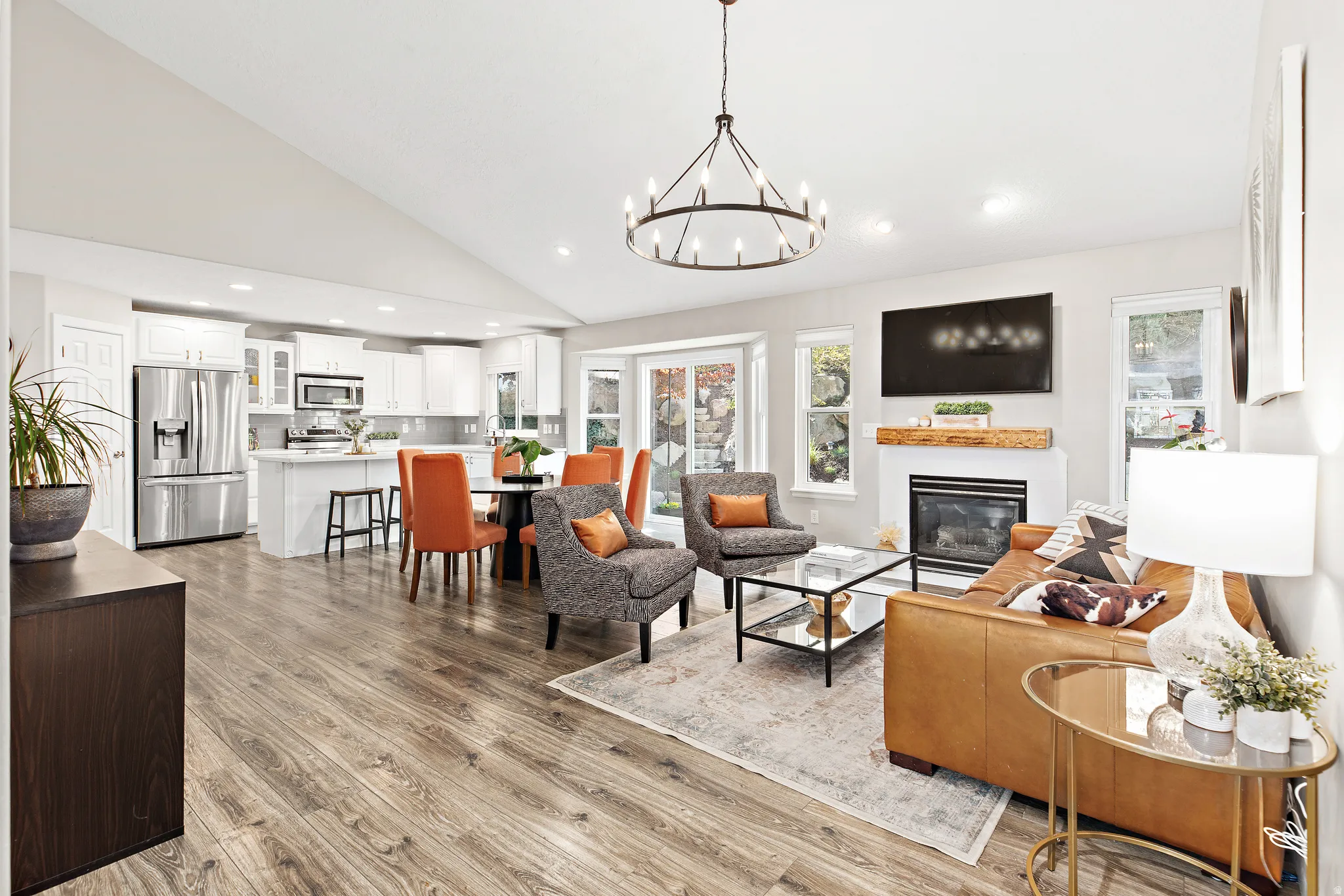 Vaulted ceilings, wood-finish flooring, white kitchen cabinetry with stainless steel appliances, bay window, and a fireplace with a wood mantle