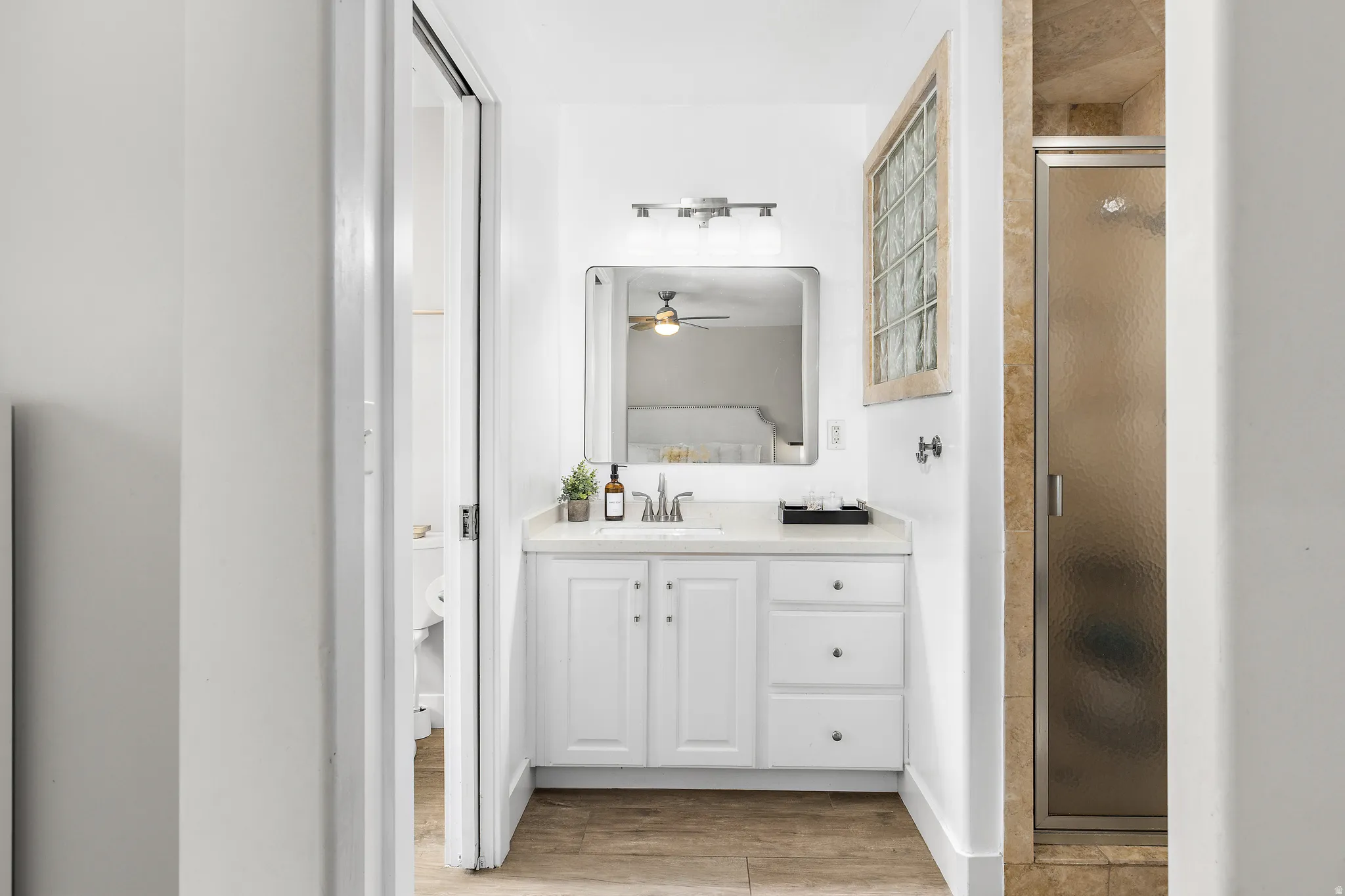 Bathroom featuring a white vanity with integrated sink, rectangular mirror, glass block window, and a shower with a framed frosted glass door