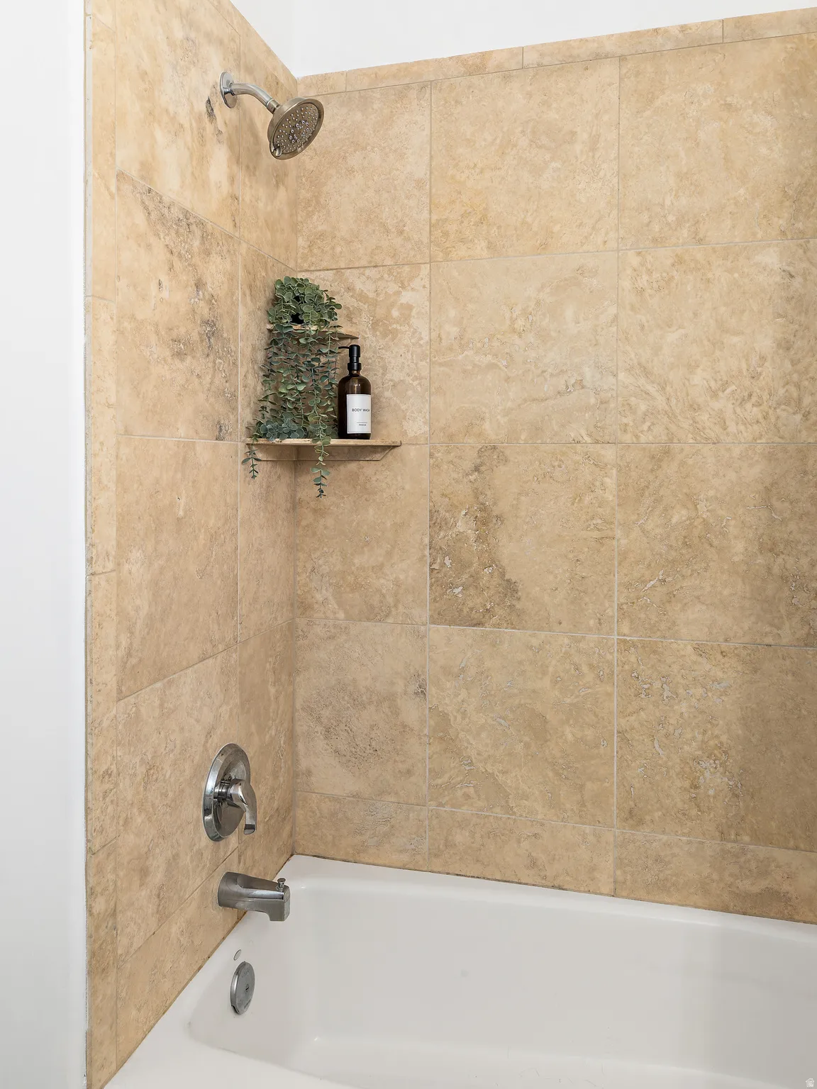 Bathtub with polished chrome fixtures, full-height wall tiling, and an integrated corner shelf