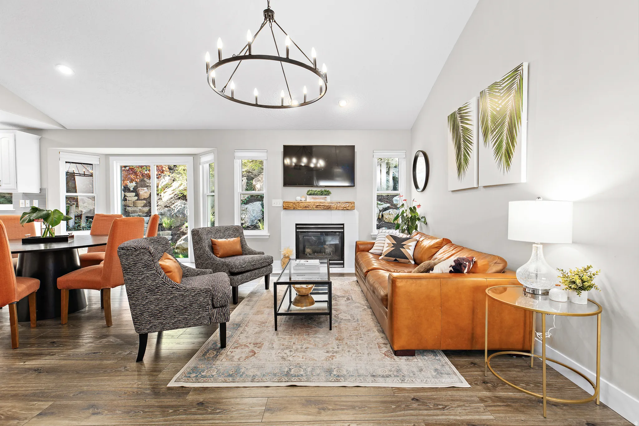Open-concept living area featuring wood-finish flooring, a fireplace with a wood mantel, a bay window, and a contemporary chandelier