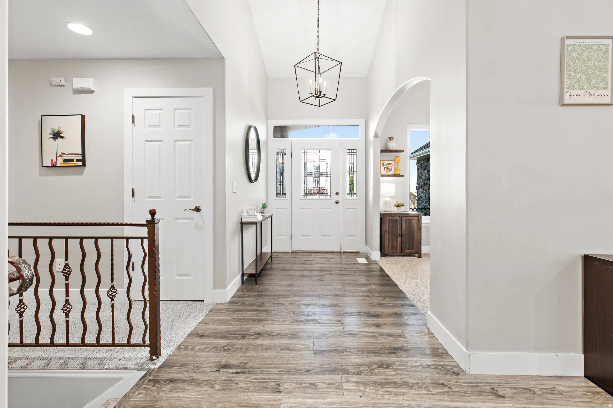 Welcoming entryway featuring a vaulted ceiling, wood-finish flooring, a decorative wrought iron railing, and an arched doorway