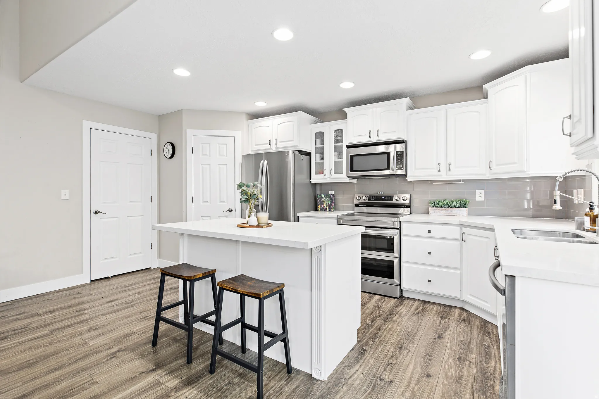 Kitchen featuring a central island, white cabinetry, integrated stainless steel appliances, light-toned countertops, and wood-finish flooring