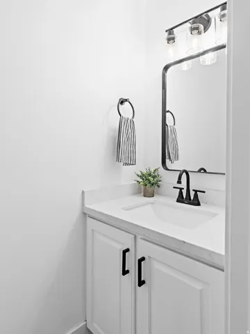 White vanity with shaker-style cabinet doors, matte black hardware, and integrated sink with a black faucet