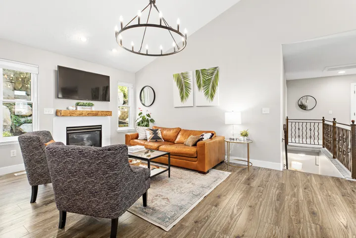 Bright, open-concept living area featuring a wood-finish plank floor, gas fireplace with built-in shelving, and an ornamental metal chandelier