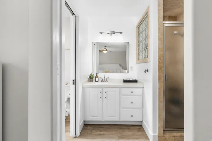 Bathroom featuring a white vanity with integrated sink, rectangular mirror, glass block window, and a shower with a framed frosted glass door