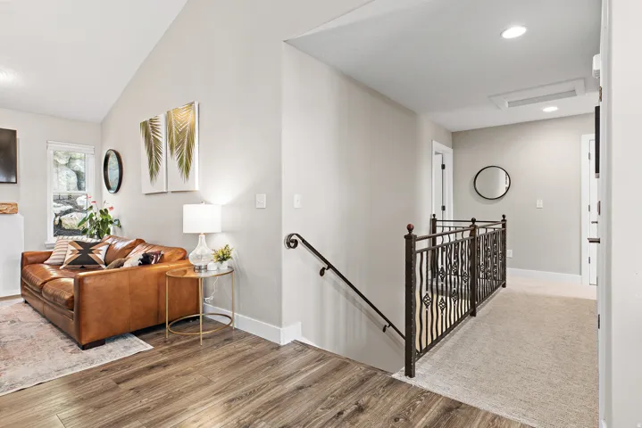Vaulted ceiling with recessed lighting, wood-finish flooring, wrought iron railing, and neutral wall tones