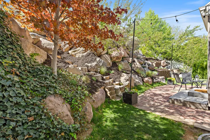 Terraced landscaping with natural rock elements, mature trees, a paver patio, and string lighting