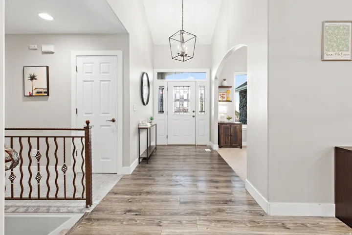 Welcoming entryway featuring a vaulted ceiling, wood-finish flooring, a decorative wrought iron railing, and an arched doorway