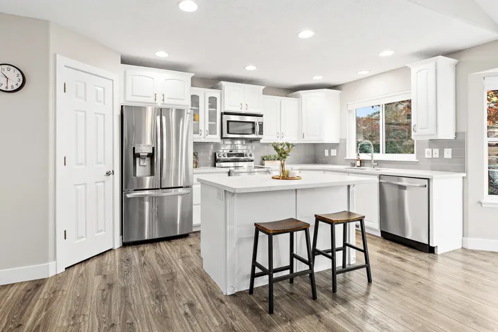 Modern kitchen featuring white cabinetry, stainless steel French-door refrigerator and dishwasher, quartz countertops, and a central island with seating