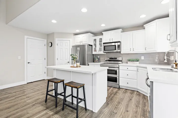 Kitchen featuring a central island, white cabinetry, integrated stainless steel appliances, light-toned countertops, and wood-finish flooring