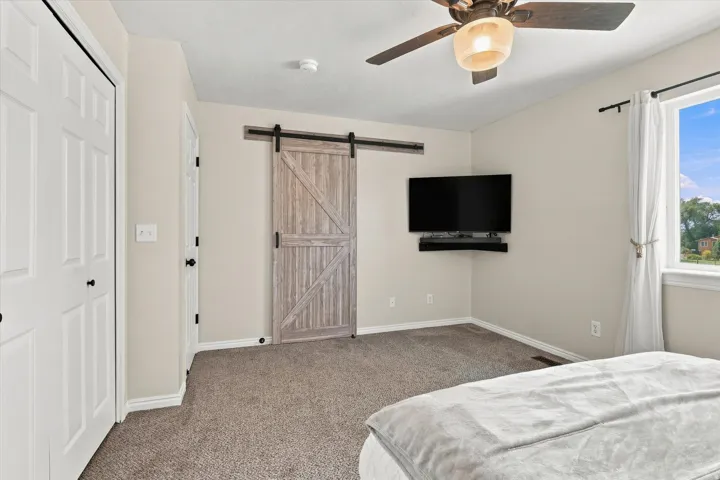 Carpeted room featuring a ceiling fan, a window with white trim, and a wood-finish barn door