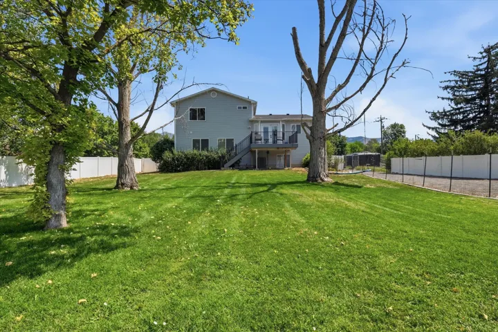 Expansive grass lawn with mature trees, fenced perimeter, and multi-story home featuring a second-level balcony