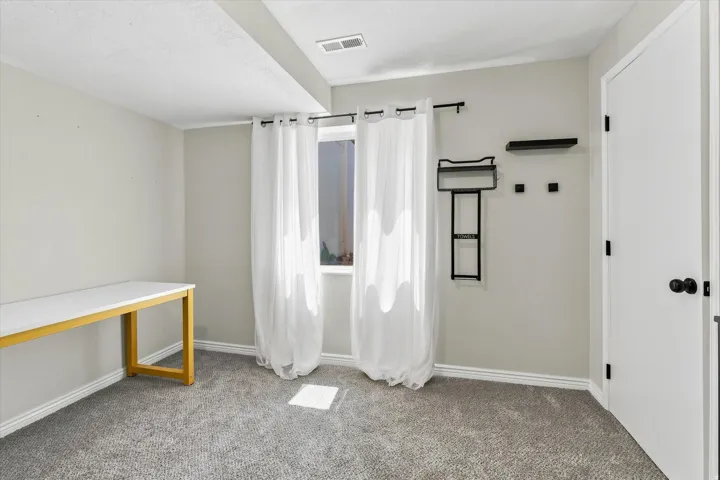 Light gray wall paint, gray carpeting, a window, and a white door with black hardware