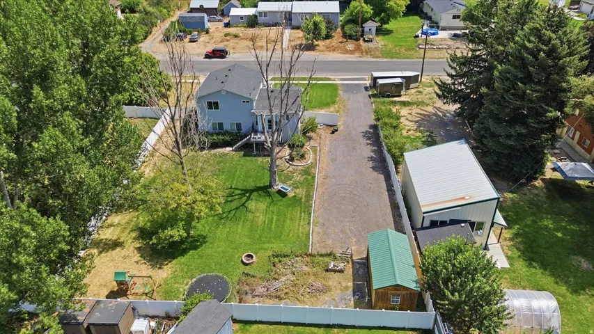 Expansive property featuring a two-story residence with a light blue exterior, a detached metal-sided building, a separate storage shed with a green roof, a large gravel driveway, and a spacious grassy yard