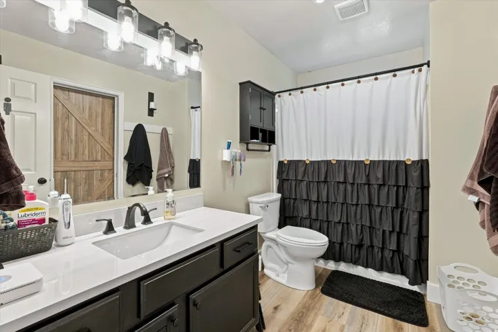 Spacious bathroom featuring a dark wood-finish vanity with a white countertop, modern lighting fixture, and wood-finish flooring