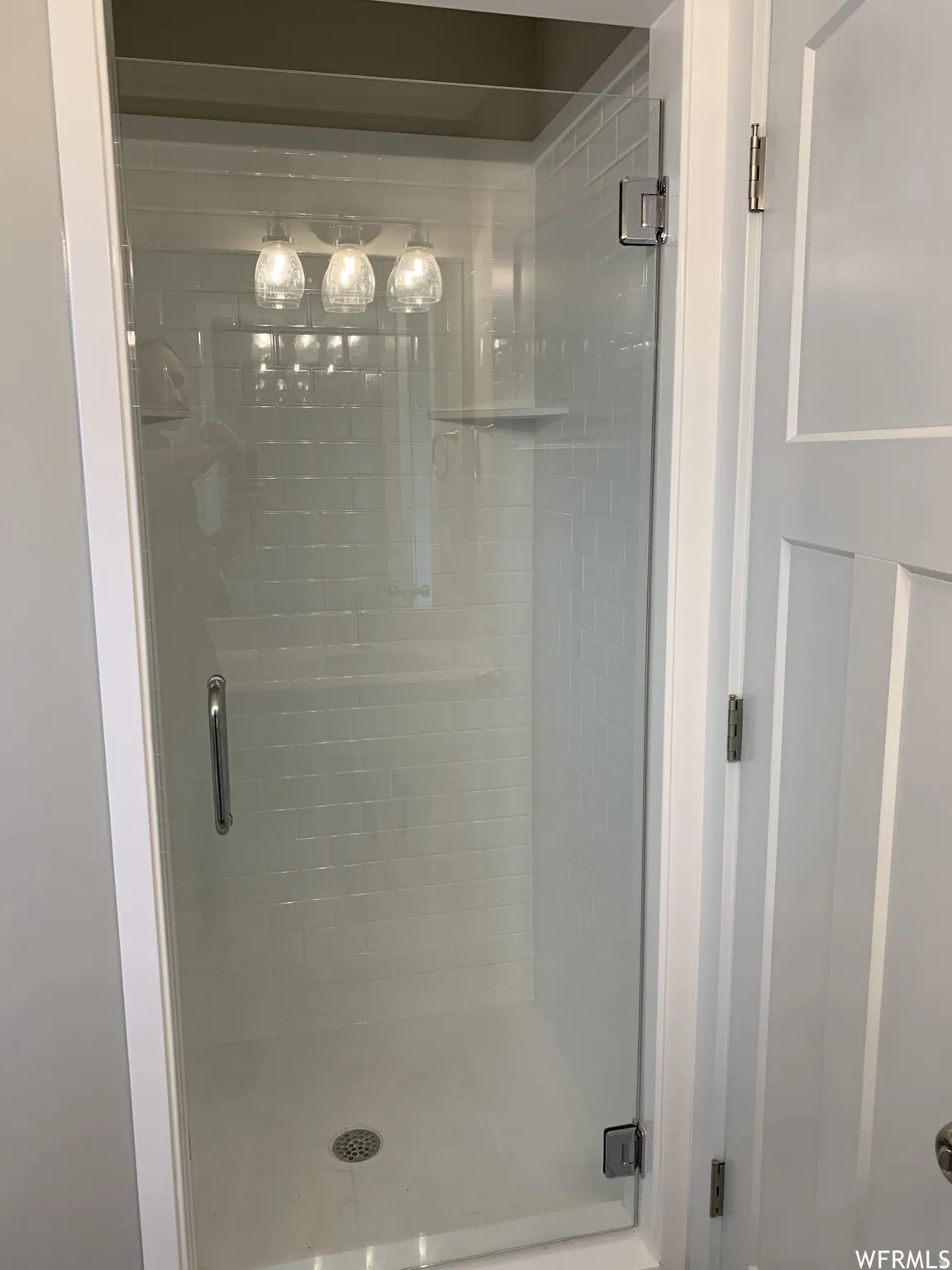 Glass-enclosed shower featuring subway tile, a built-in shelf, and a triple light fixture