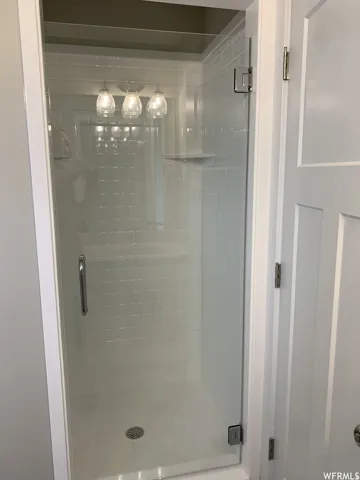 Glass-enclosed shower featuring subway tile, a built-in shelf, and a triple light fixture