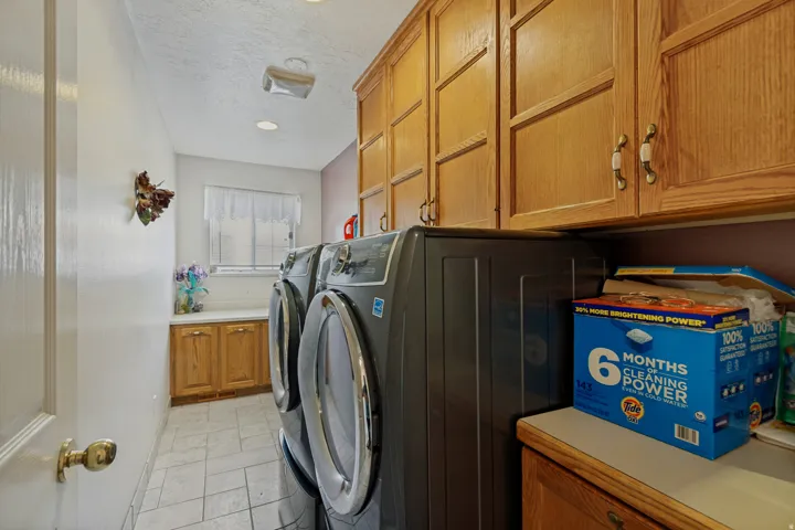 Laundry area featuring overhead cabinetry, built-in lower cabinetry, a counter surface, a window, and tile flooring