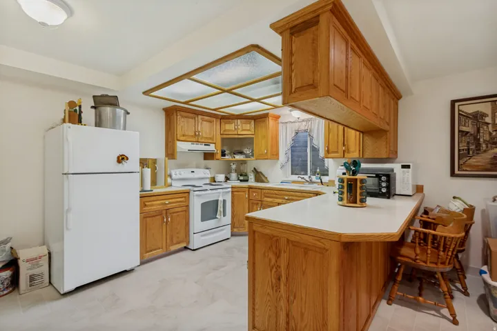 Kitchen featuring wood-finish cabinetry, white countertops, a breakfast bar, recessed lighting, and white appliances
