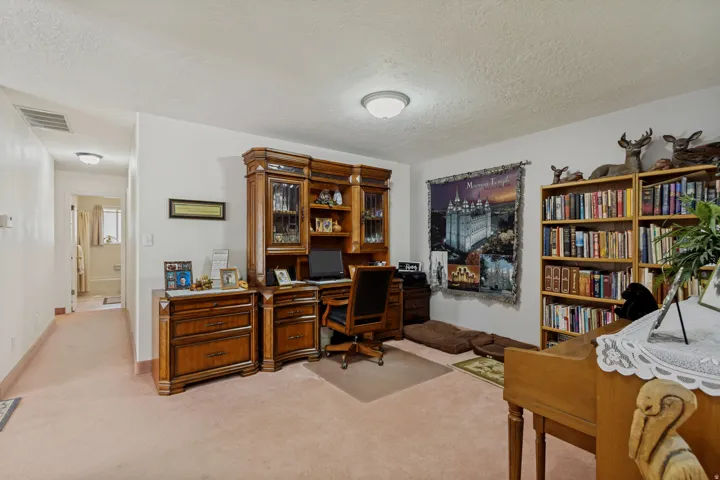 Versatile home office and library space featuring custom wood cabinetry with glass-front display doors, built-in desk with ample work surface, wall-to-wall shelving with substantial book storage capacity, plush carpeting throughout, and recessed ceiling l