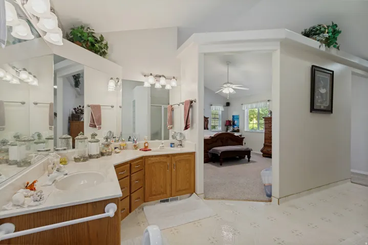 Spa-inspired primary bathroom featuring dual vanities with wood cabinetry, marble countertops, large framed mirrors with integrated lighting, and tile flooring