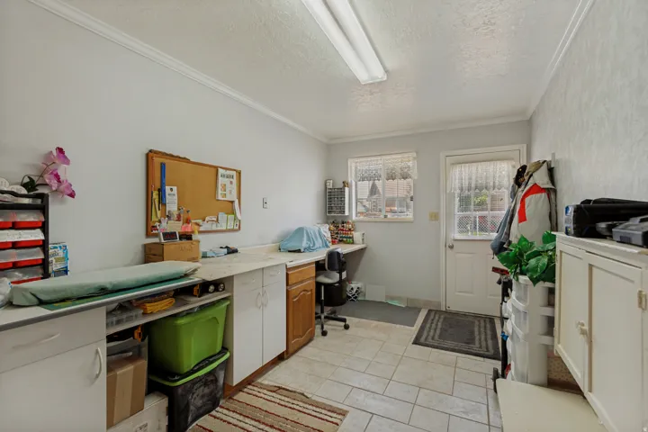 Functional workspace featuring tile flooring, ample cabinetry with wood-finish doors, built-in countertop workspace with multiple storage solutions, large windows providing natural light, and a door providing exterior access