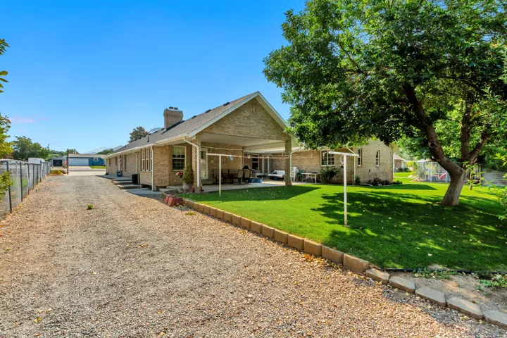 Gravel driveway, brick exterior, covered patio, lush lawn, and mature trees