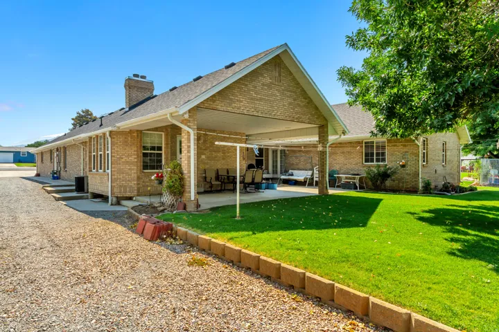 Spacious backyard featuring a covered patio, extensive gravel driveway, brick exterior, and a well-maintained lawn