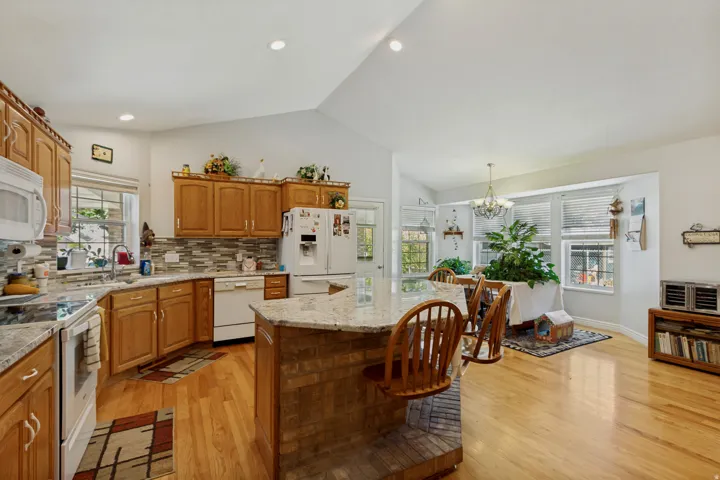 Spacious kitchen featuring warm wood cabinetry, granite countertops, stainless steel appliances, a large center island with seating, and abundant natural light from multiple windows