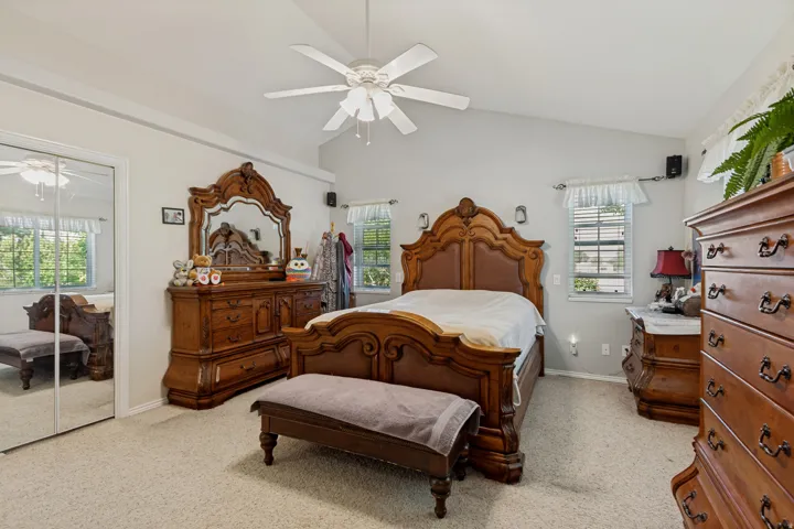 Vaulted ceiling, ceiling fan, carpet flooring, mirrored closet doors, and multiple windows with blinds