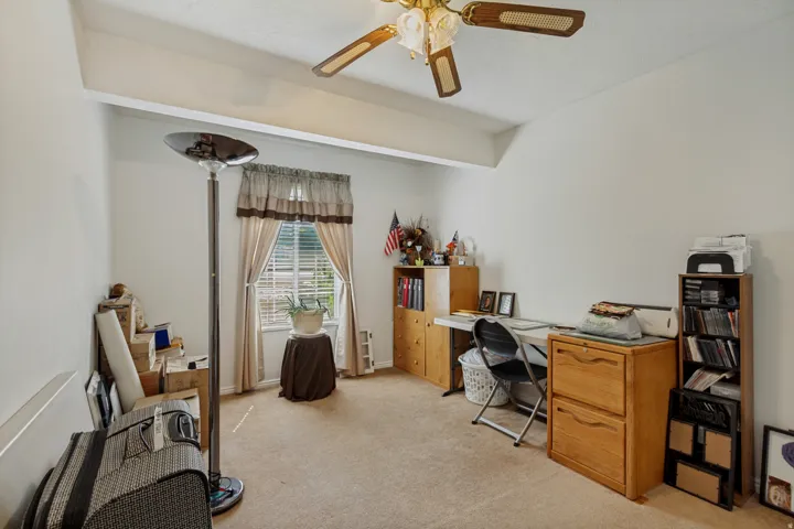 Versatile bonus room featuring neutral carpeting, abundant natural light from shuttered windows, ceiling fan with brass finish, and ample built-in storage cabinetry