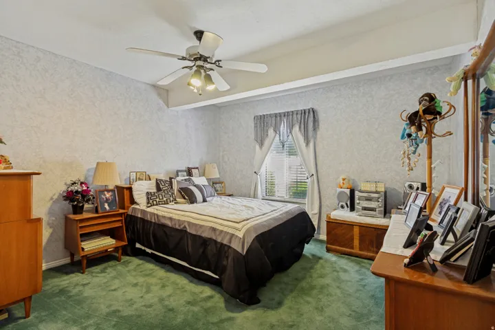 Sloped ceiling with ceiling fan light fixture, window with blinds, and green carpet flooring