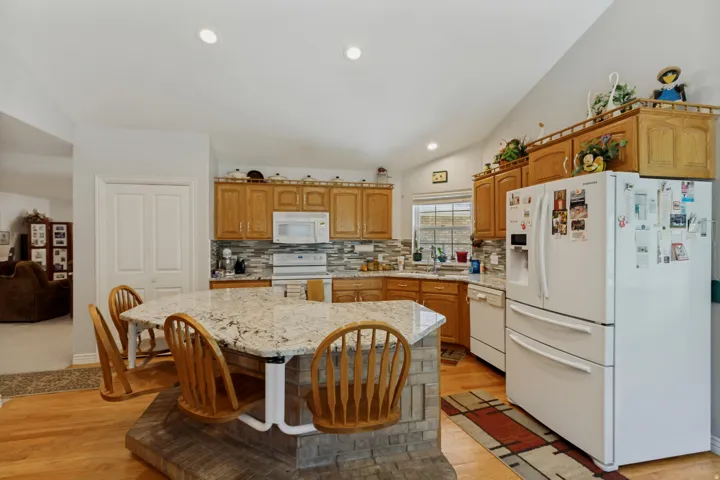 Spacious kitchen featuring wood cabinetry, stainless steel appliances including a double-door refrigerator, tile backsplash, and a large island with stone countertop and seating
