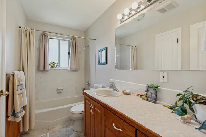 Spa-inspired primary bathroom featuring a wood-finish vanity with dual-sink layout, quartz countertop, and polished chrome hardware