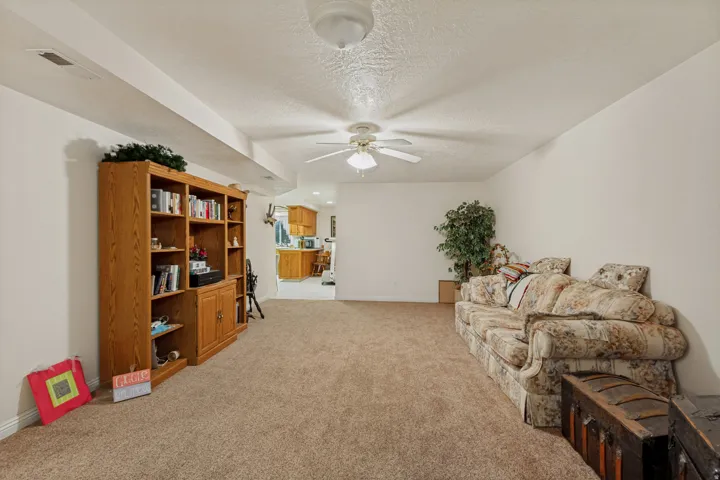 Spacious recreation room featuring neutral carpet flooring, wood-finish cabinetry with built-in shelving and storage, ceiling fan with integrated lighting, and abundant natural light from recessed fixtures