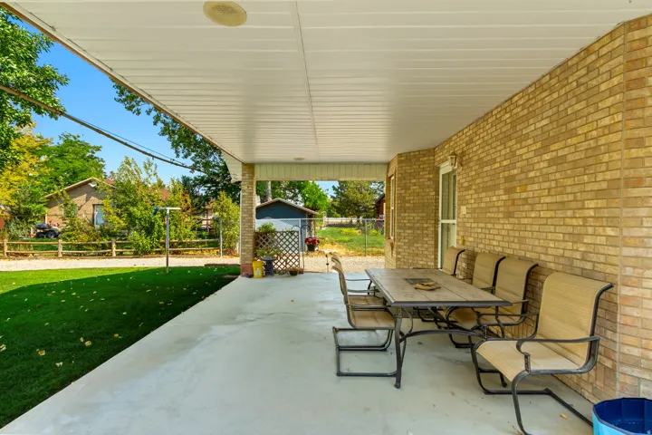 Expansive covered patio with a white ceiling and brick exterior, overlooking a manicured lawn with mature landscaping