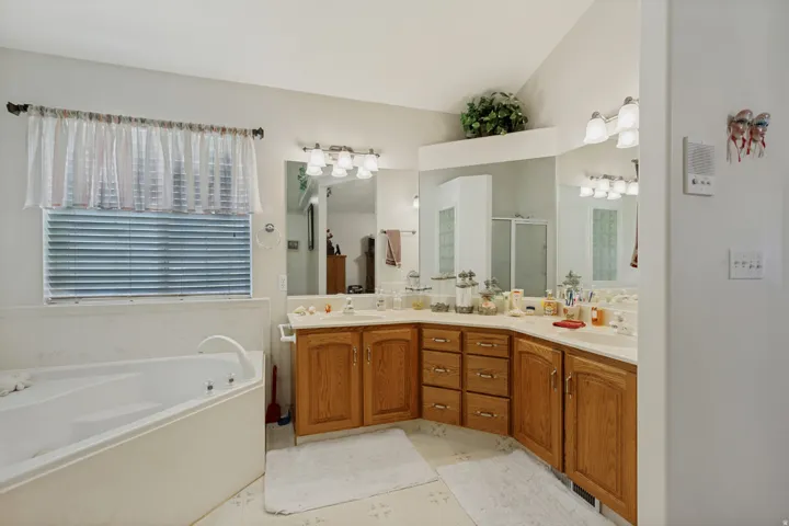 Corner soaking tub, dual vanity with wood-finish cabinetry, integrated sinks, large mirrors, and wall-mounted light fixtures