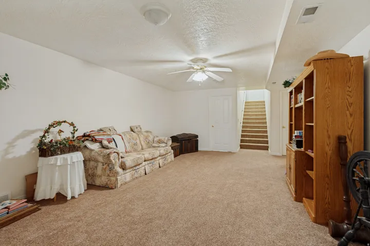 Spacious finished basement with neutral carpet flooring, ceiling fan with integrated lighting, built-in wood cabinetry with open shelving, and direct staircase access to upper levels